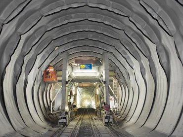 Foto: Abdichtung Wienerwaldtunnel: Blick in Längsrichtung in den Tunnel; die PVC-Dichtungsbahnen werden gerade verlegt und liegen wie eine Reihe von grauen Reifen innen an der Tunnelwand