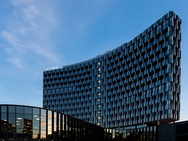 Foto: Styria Media Center: Abendstimmung, geschwungene Glasfassade des Hochbauses und gläserner Flachbau im Vordergrund