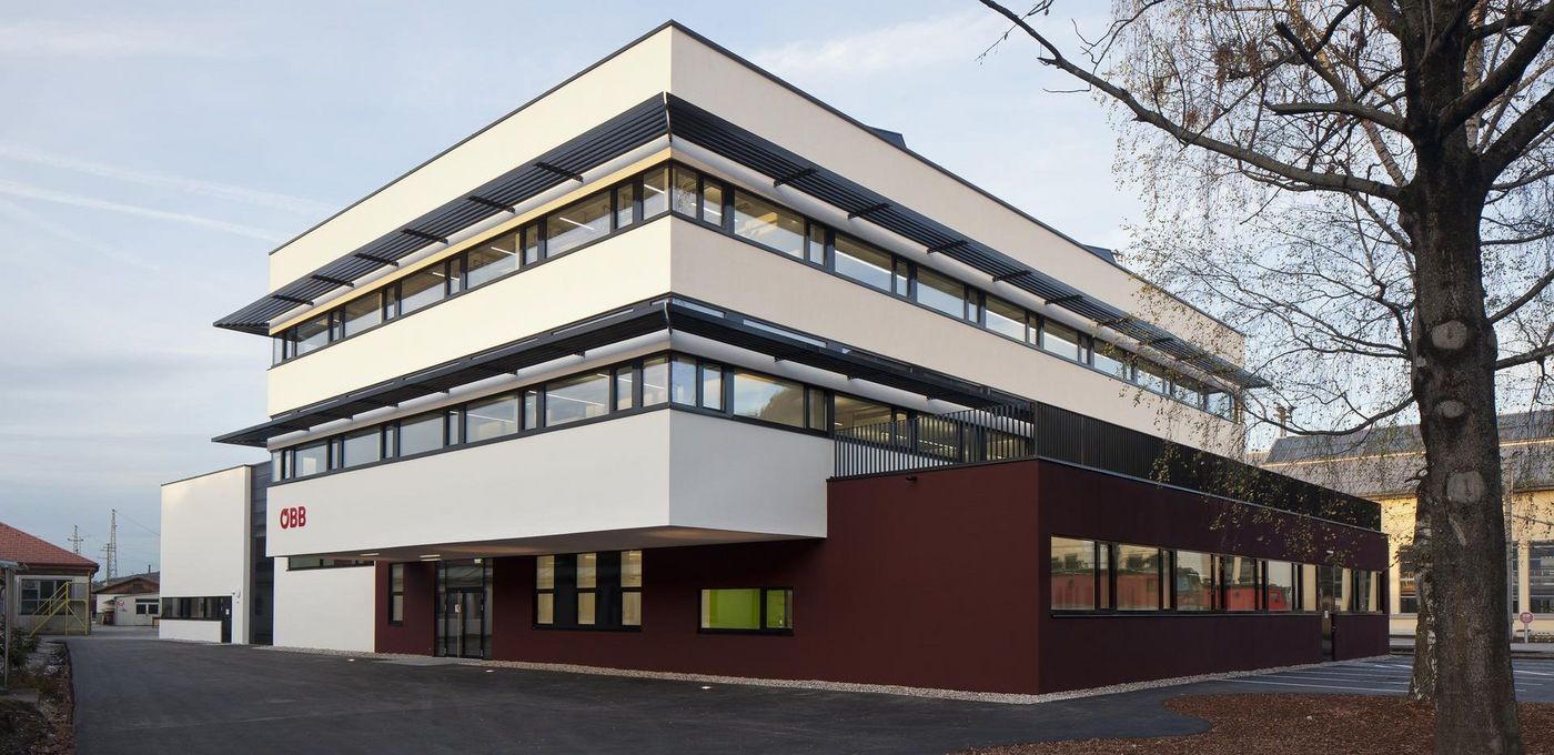 Foto: ÖBB Lehrwerkstätte: Perspektivische Ansicht der Fassade: Dunkelbraune Färbung im Erdgeschoss und weißer Verputz in den Obergeschossen
