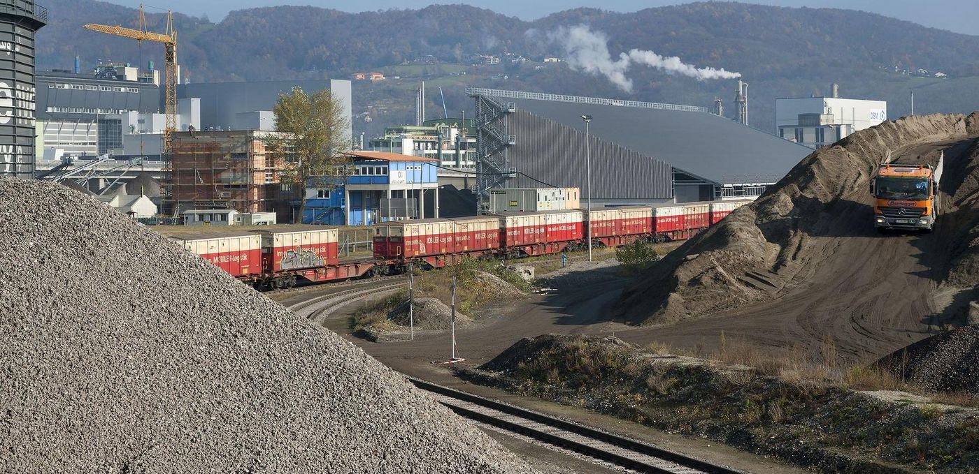 Photo: Linz coke plant: view of the area to be remediated; a train on the left in the background and factory halls behind it; a lorry on the right