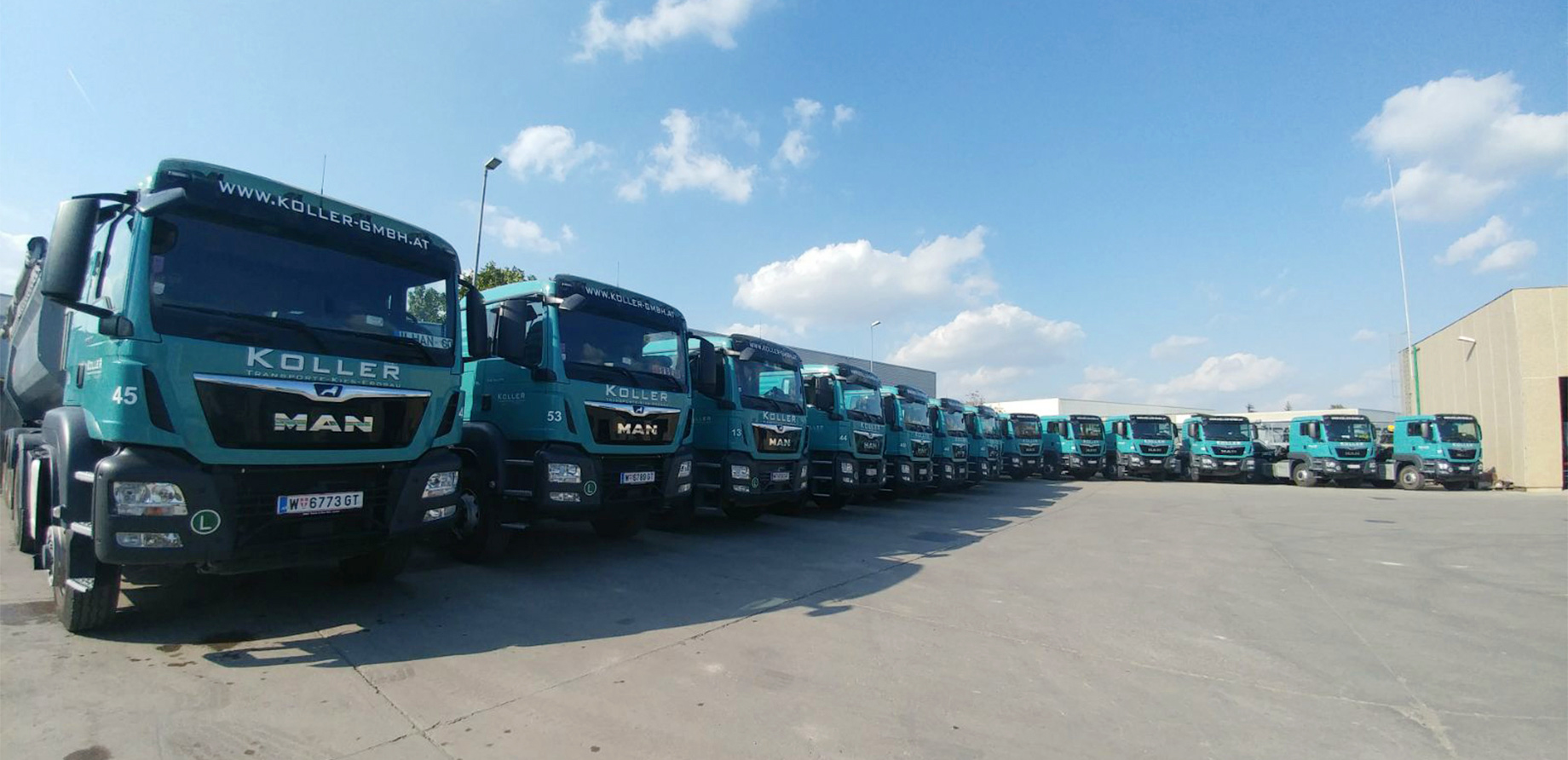 Photo: A good dozen lorries parked next to each other in an L-shape on a large asphalt concrete surface; a logistics warehouse in the background